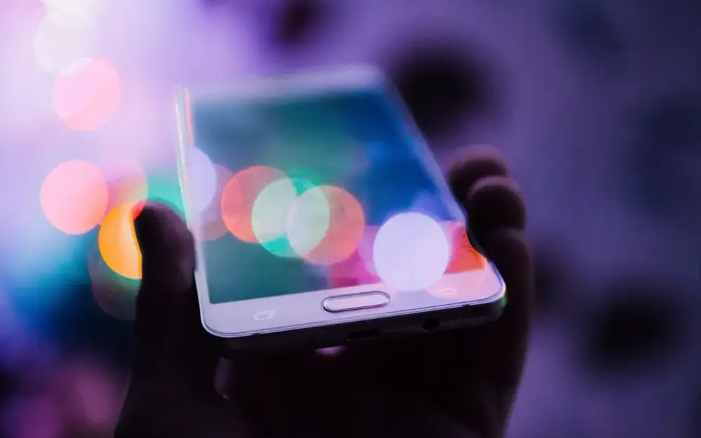 Hand holding a smartphone with colourful bokeh lights
